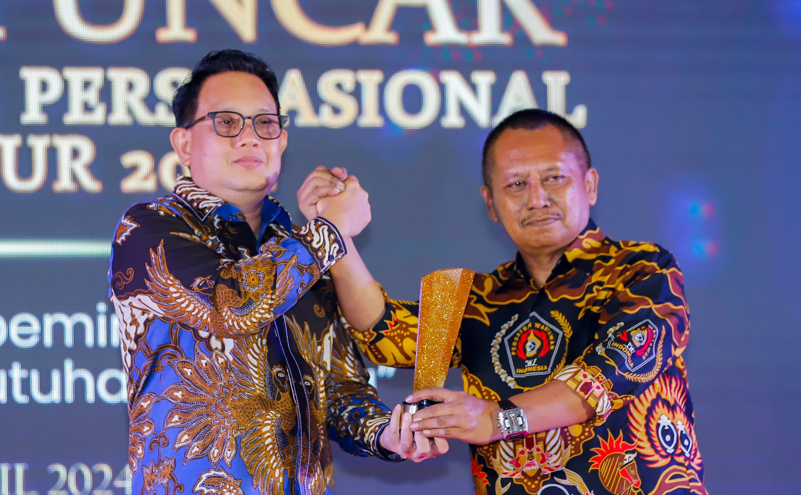 Pj Gubernur Jatim Adhy Karyono (kaca mata) menerima PWI Jatim Award 2024 dari Ketua PWI Jatim Lutfil Hakim. (Istimewa)